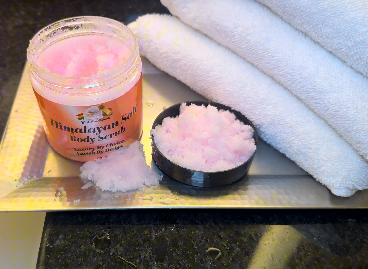 A jar of pink Himalayan salt body scrub is open with some product spilled out onto a surface next to a black dish and a white towel.