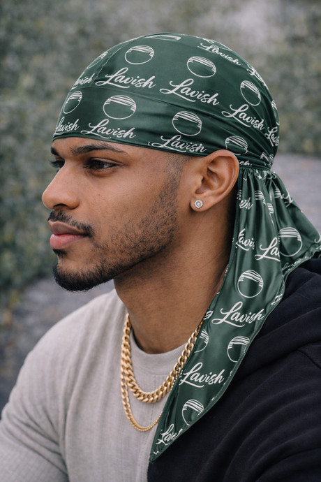 Man wearing a green bandana with 'Lavish' branding, sitting against a stone wall.